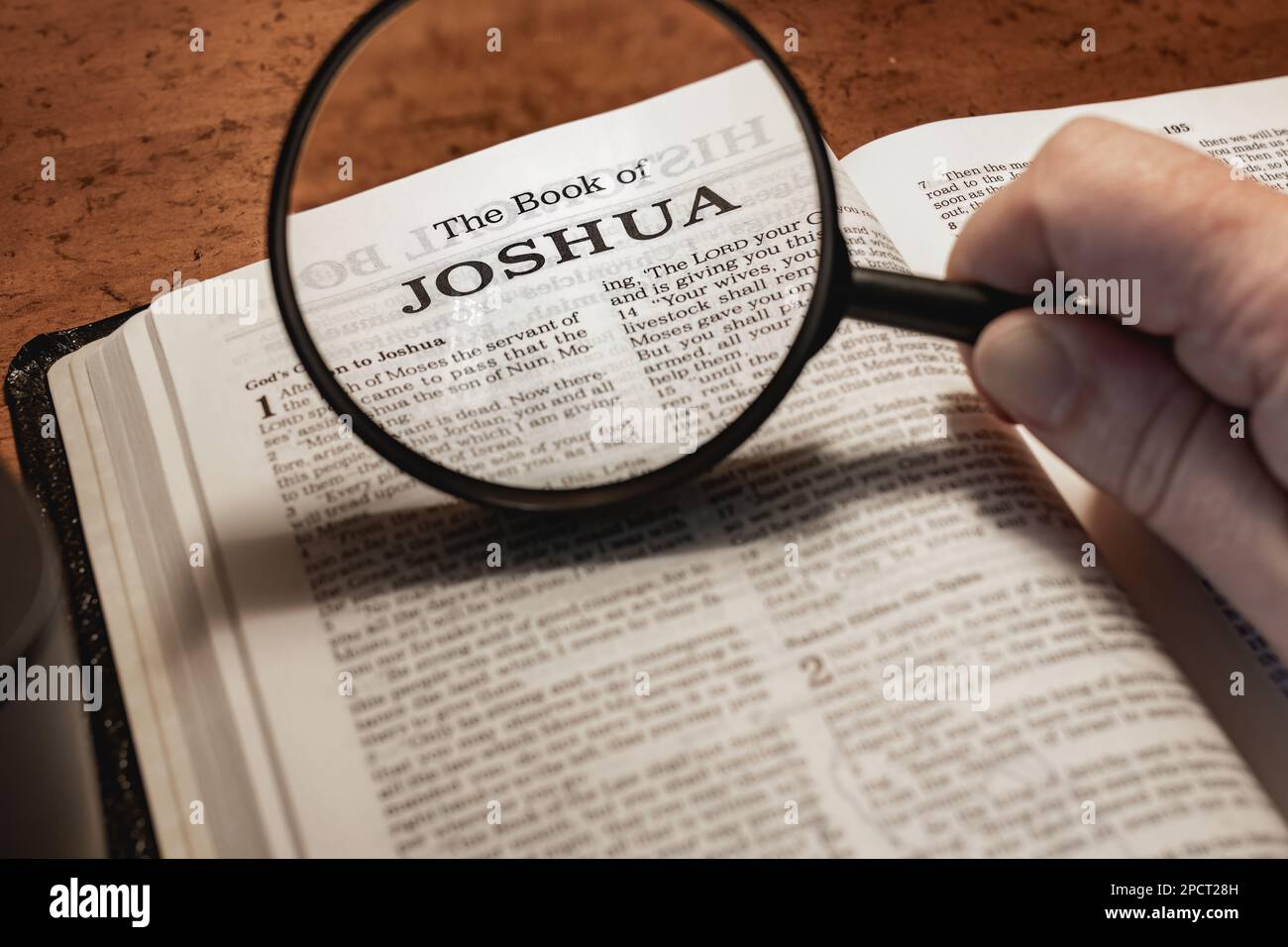A closeup of a person holding a magnifier and reading the book of Joshua  from the New Testament Stock Photo - Alamy