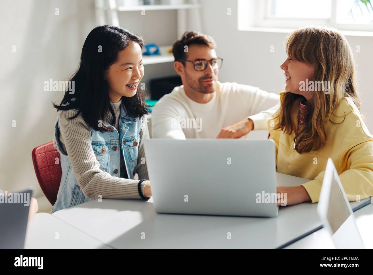Tutor helping young female students with a computer science lesson in a classroom. Two young girls smiling and engaging with their teacher as they lea Stock Photo