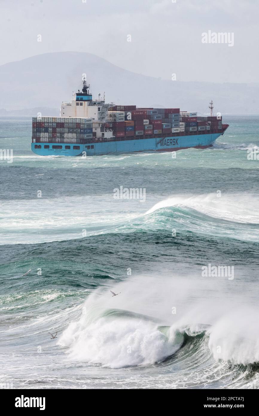 A giant cargo ship sailing across the rough pacific ocean with waves crashing off the coast of New Zealand. Stock Photo