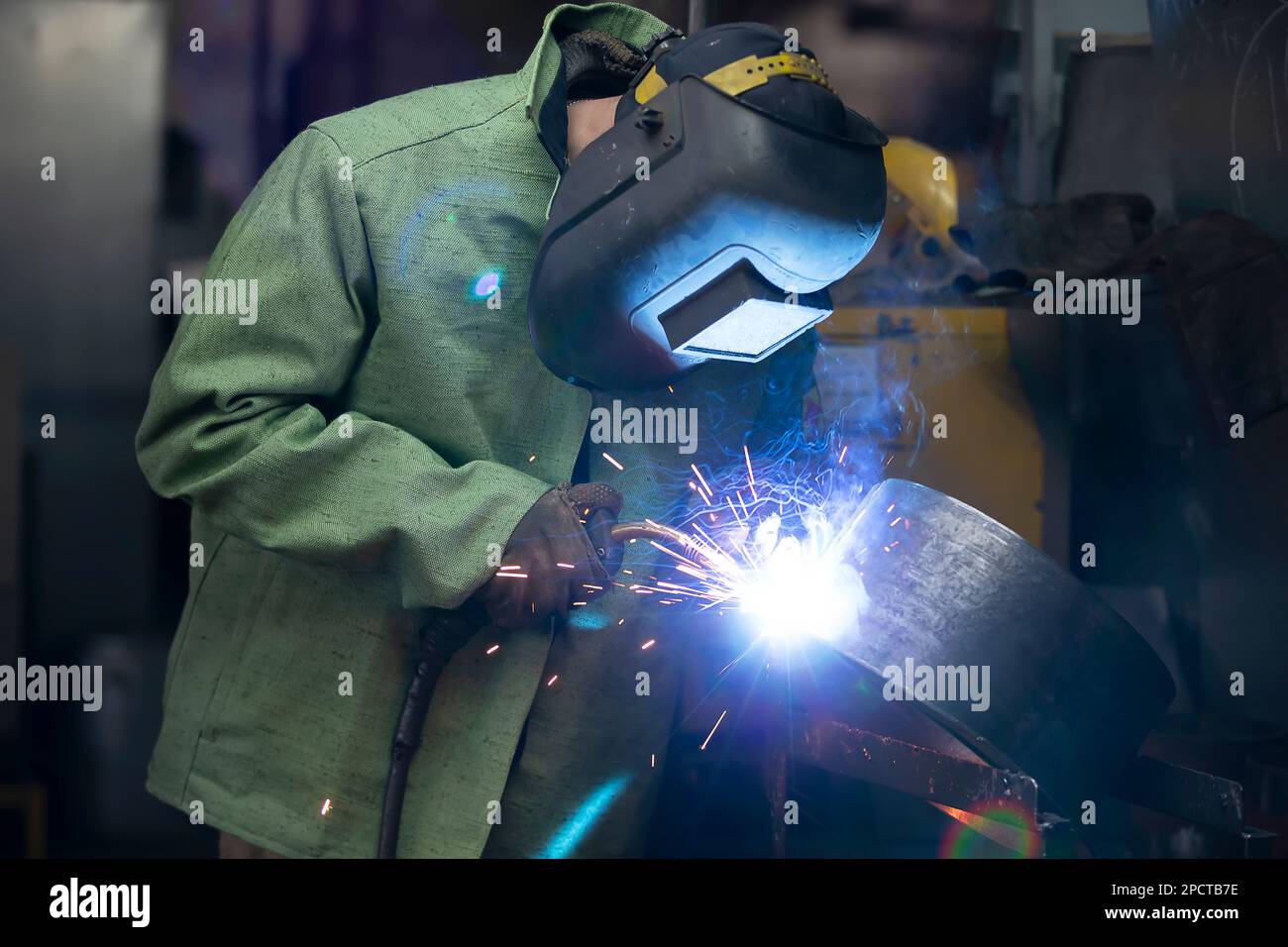 Welder in a protective mask works and sparks fly flame Stock Photo