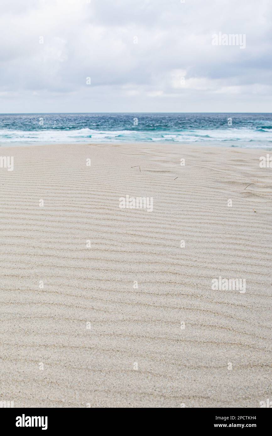 White sand dune and the patterns of ripples in the sand with the pacific ocean behind, a minimalist scene in Aotearoa New Zealand. Stock Photo
