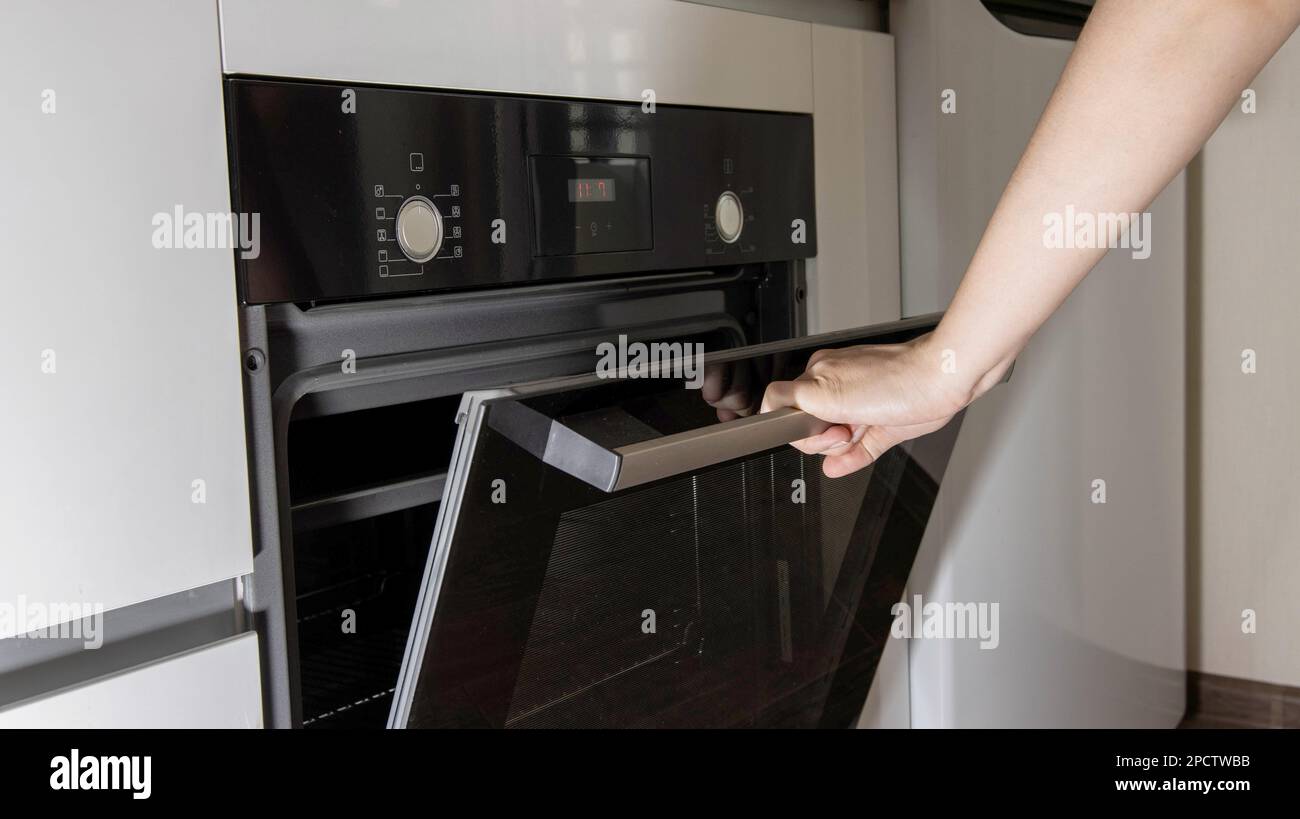 A woman's hand opens the door of a modern oven in the kitchen