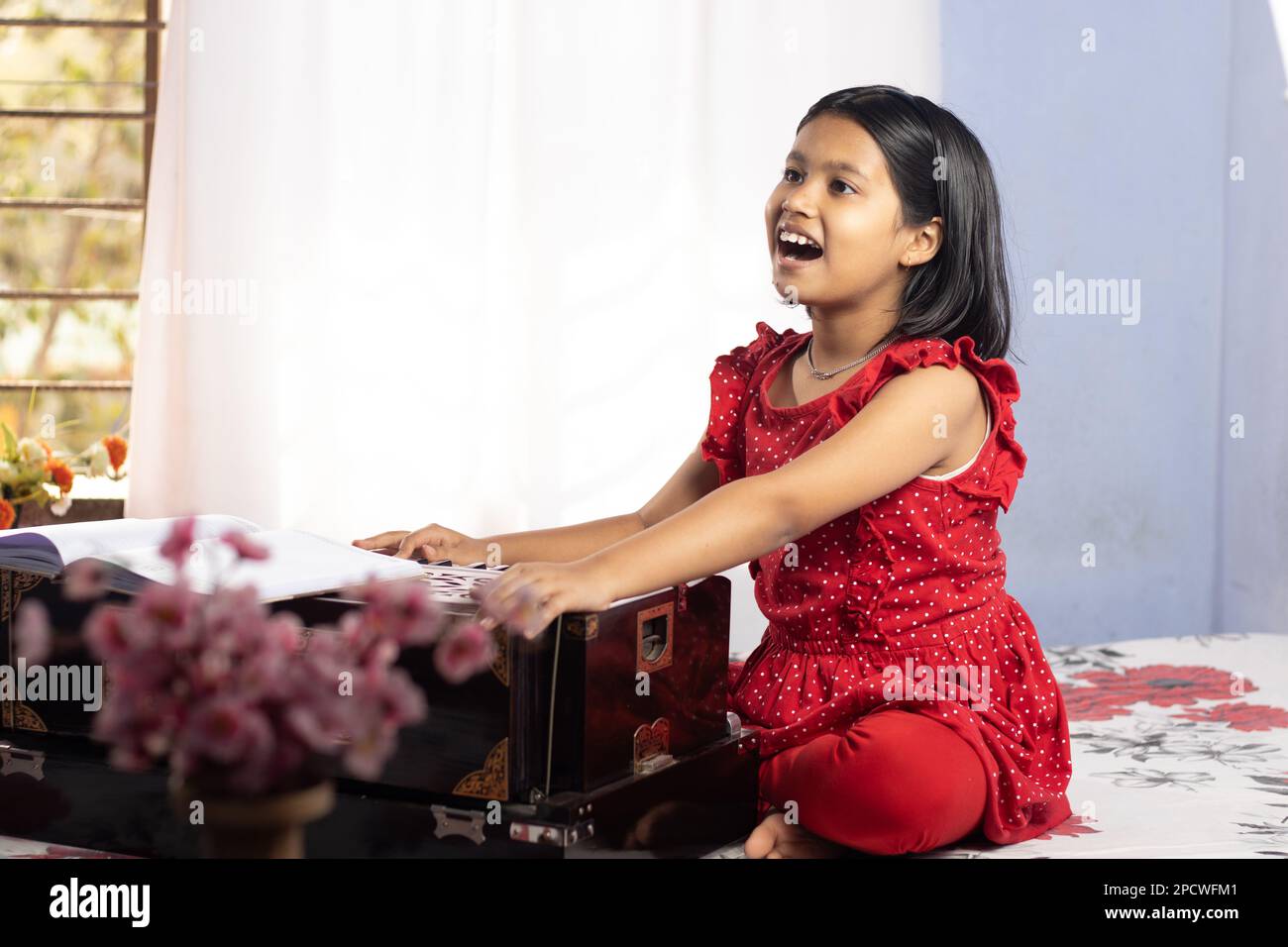 An Indian cute girl child singing and playing harmonium on white
