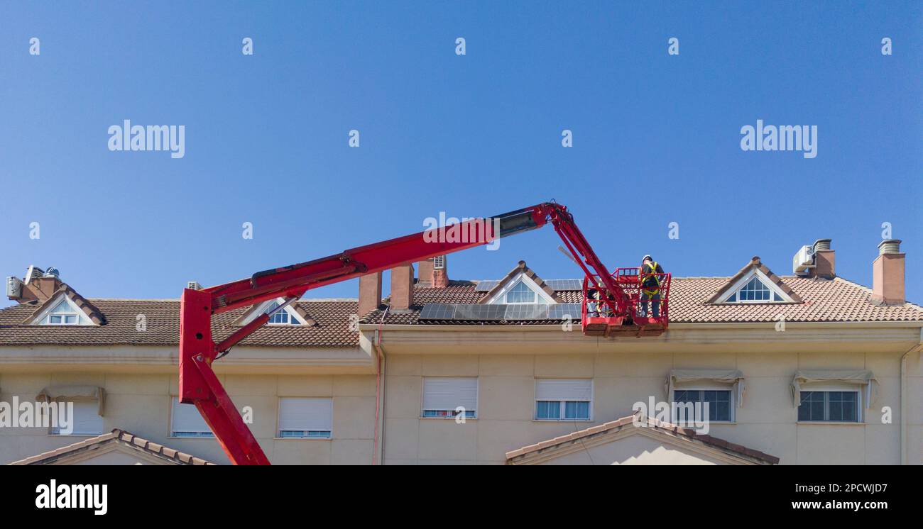 Workmen installing solar panels on the roof of a terraced house. They working over articulated boom lift Stock Photo