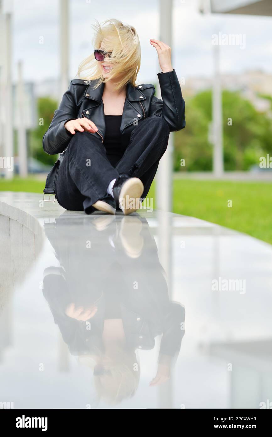 Girl in black clothes sits on railing in windy day Stock Photo