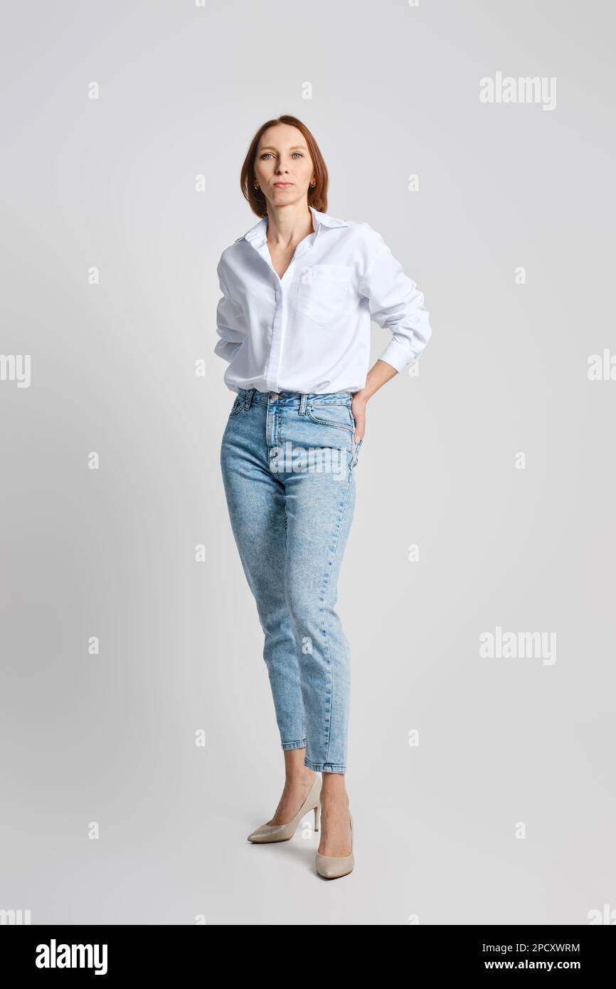 Attractive middle aged woman in white shirt put palms of her hands in back  pockets of her blue jeans Stock Photo - Alamy