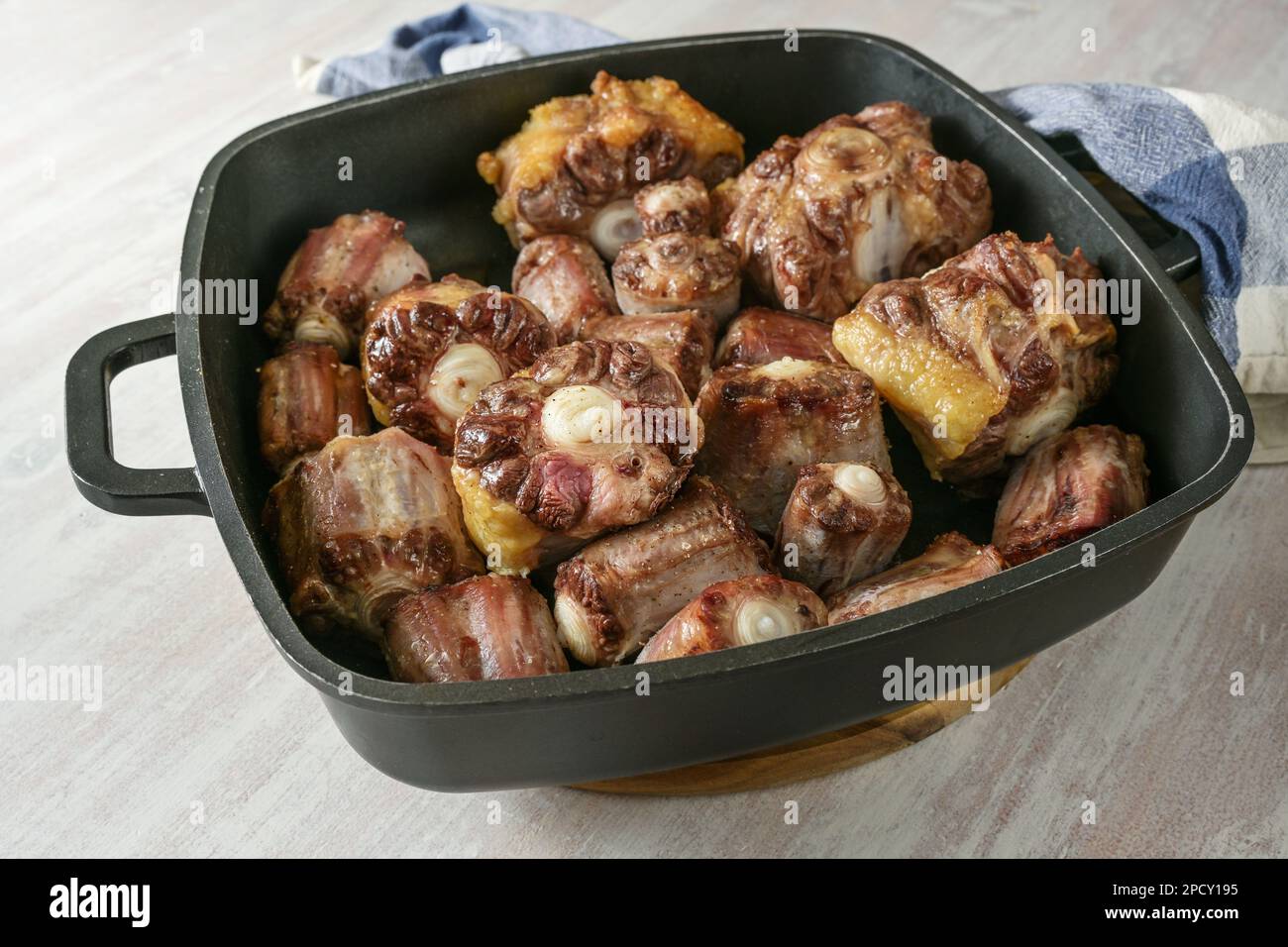 Roasted oxtail pieces with bone in a black tray fresh from the oven, gelatin-rich meat for a slow-cooking stew or traditional oxtail soup, copy space, Stock Photo