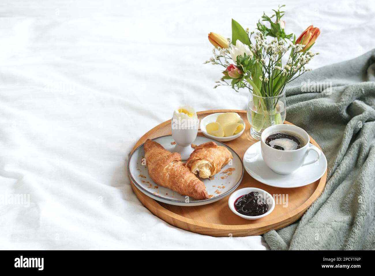 Sunday breakfast in bed with coffee, croissant, jam and boiled egg served on a wooden tray with a bouquet of flowers on mother's day, birthday or vale Stock Photo