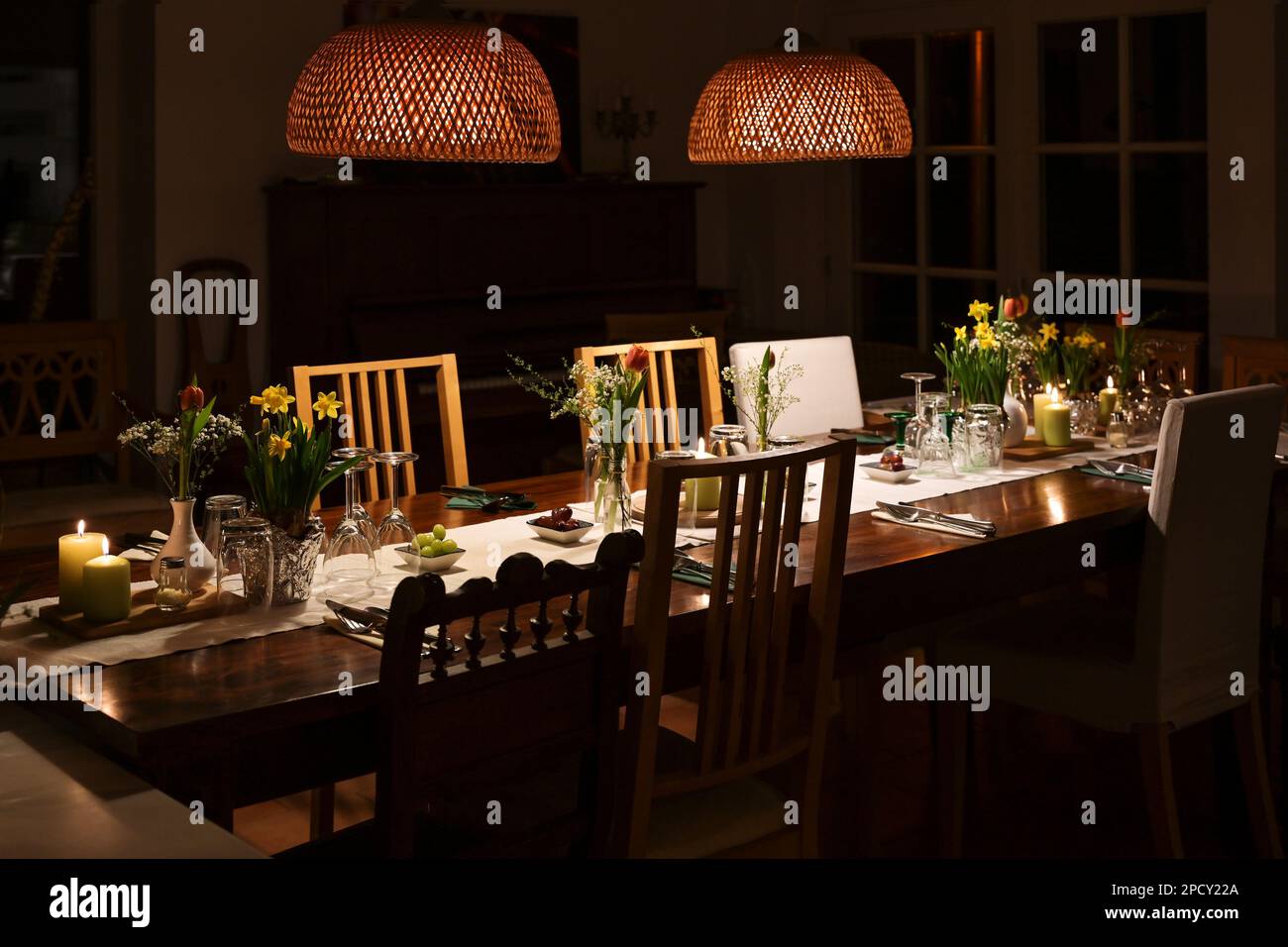 Large dining table at night decorated for a casual dinner party with family and friends with candles, spring flowers, drinking glasses and different c Stock Photo