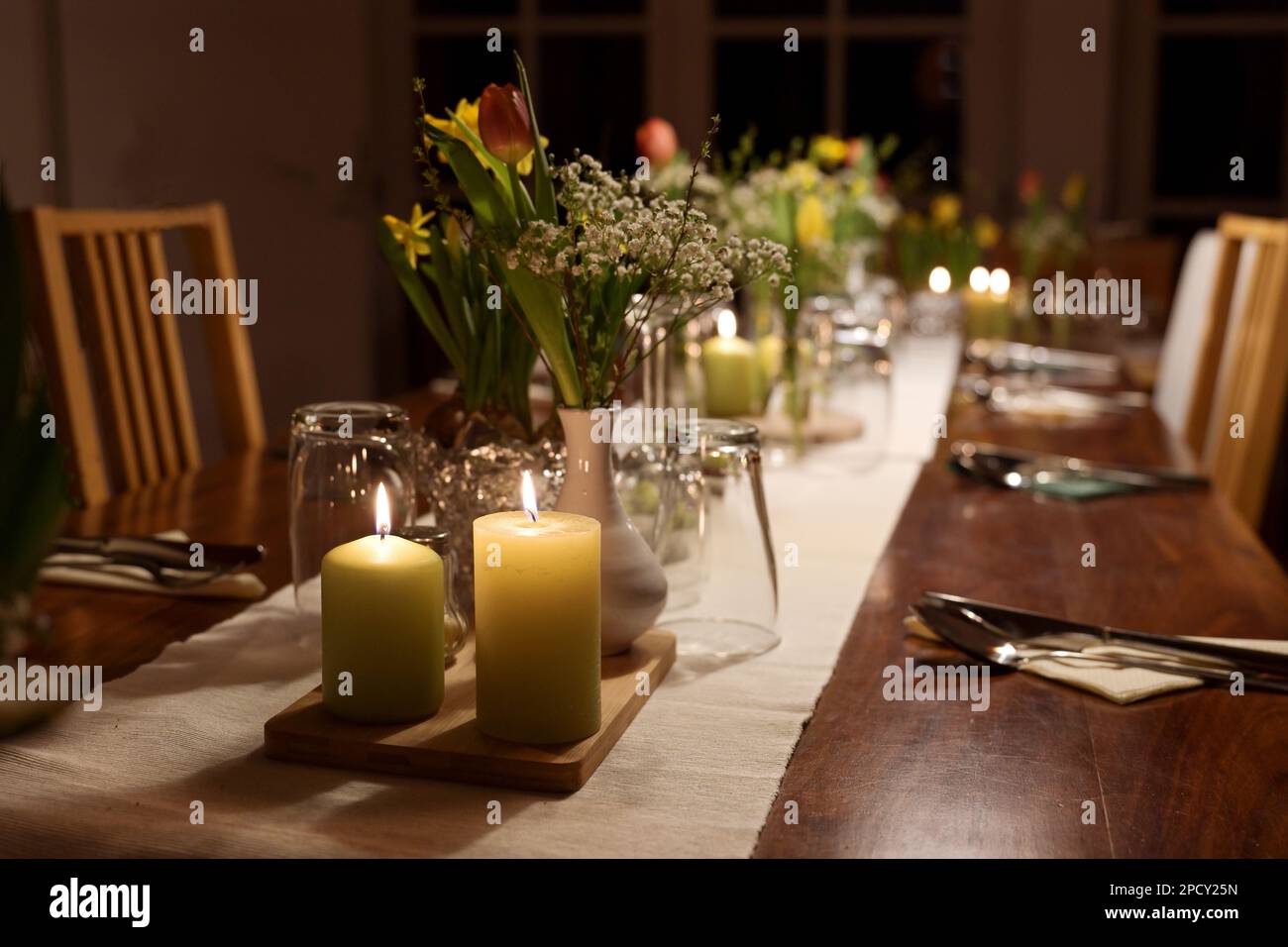 Table setting for a large dinner party with family and friends decorated with candles, spring flowers and various drinking glasses at night, selected Stock Photo