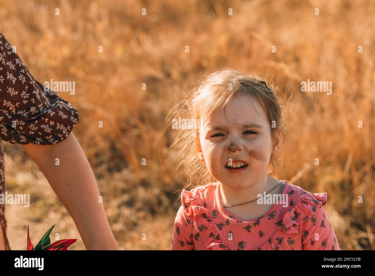 Little girl with a dirty face and dirty clothes in nature with her mom. Children playing outside with dirty hands. Stock Photo