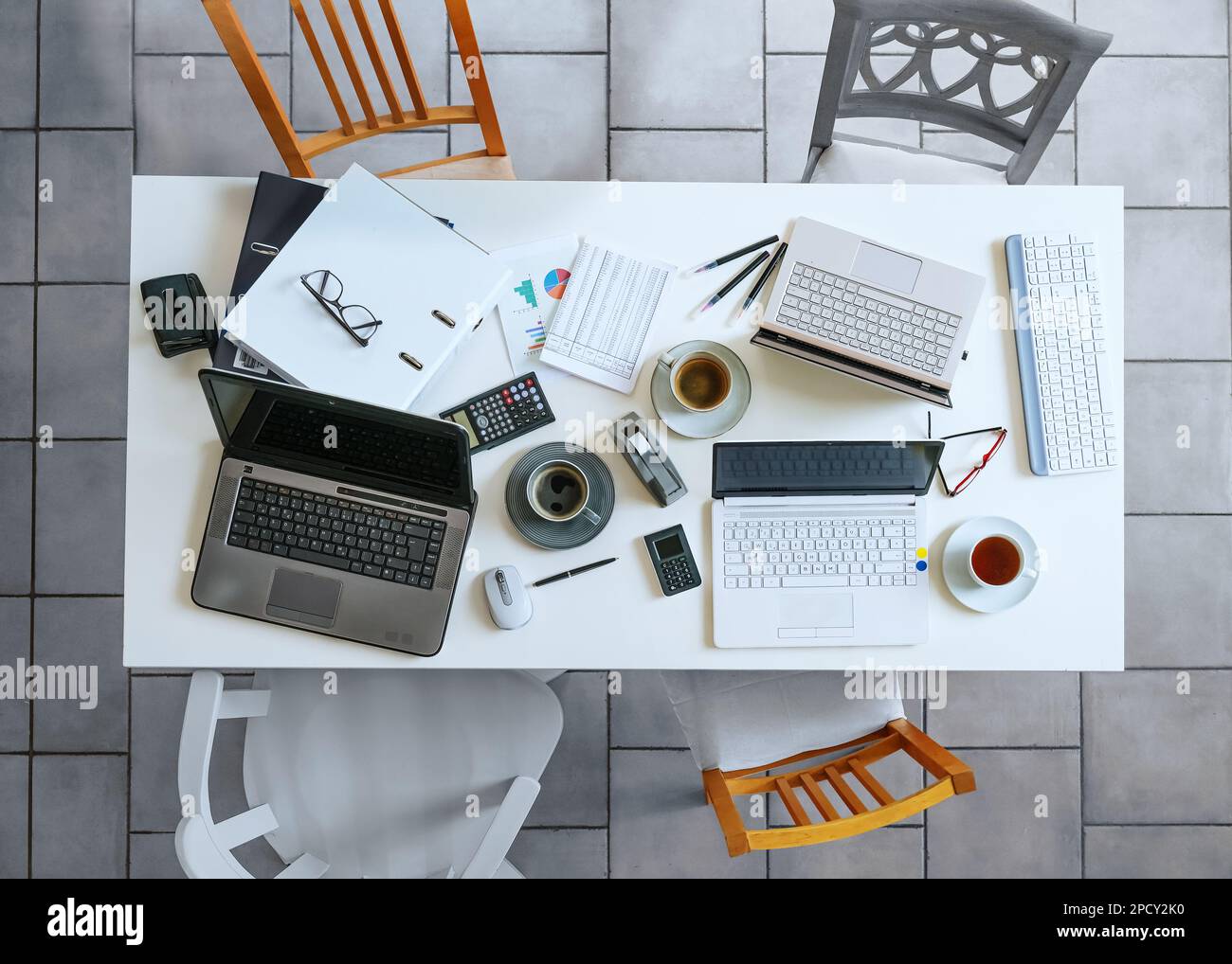 Top view of a small white meeting table with laptops, coffee, calculator, papers, ring binder and four casual chairs on a gray tiled floor business, h Stock Photo