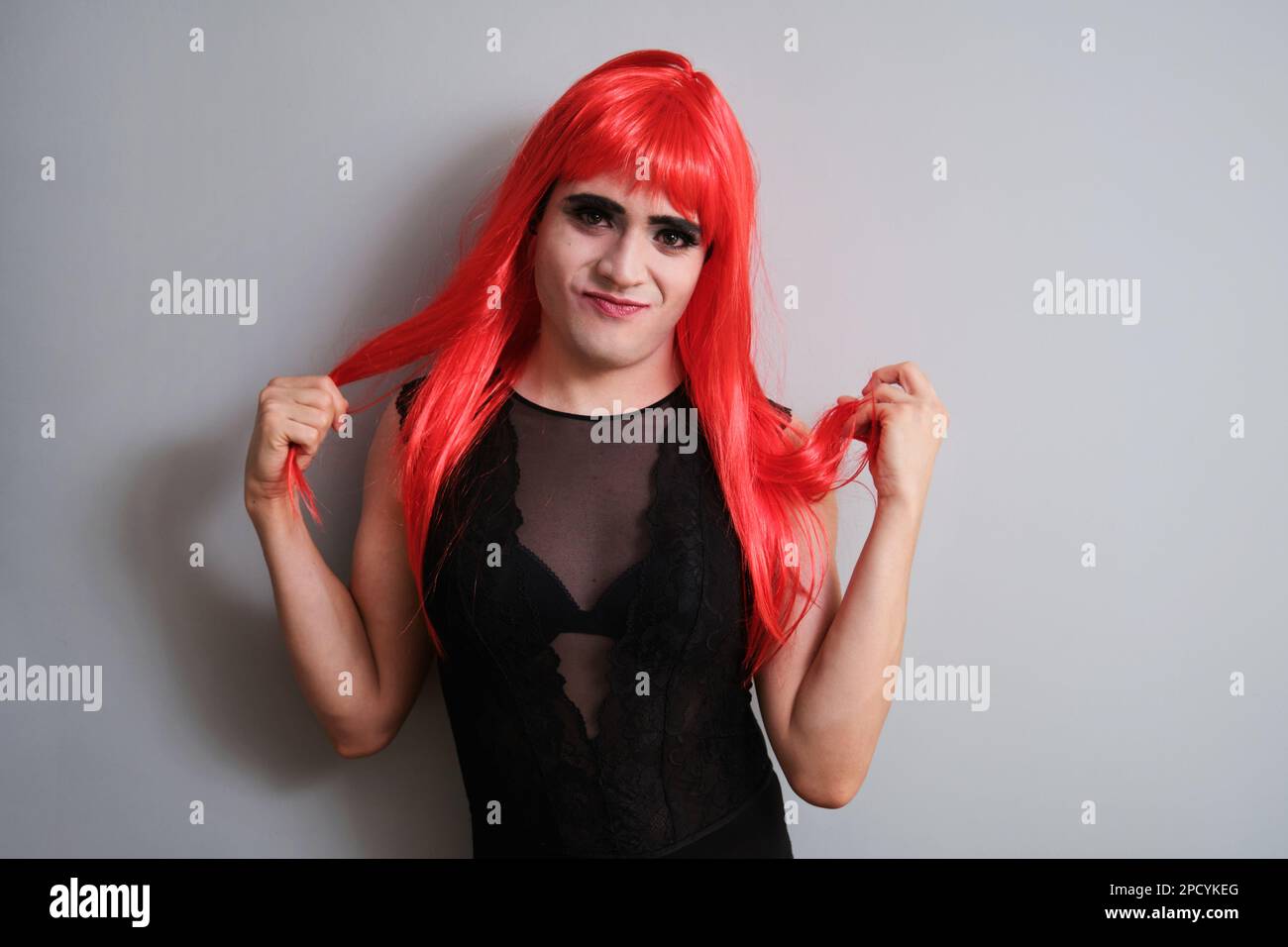 Portrait of transgender man looking at camera wearing a red wig. Stock Photo