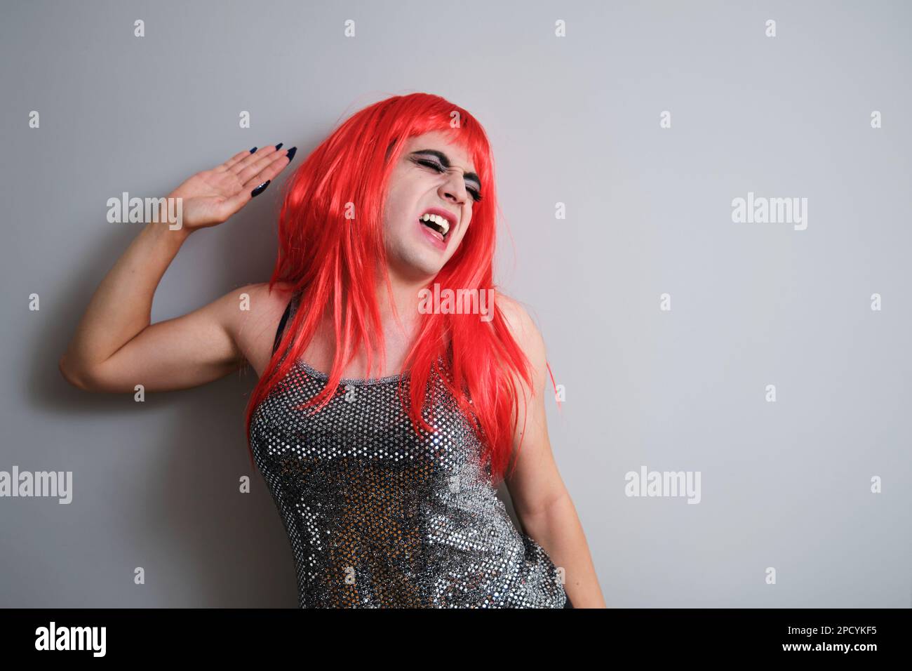 Portrait of gender fluid male screaming and wearing a red wig. Stock Photo