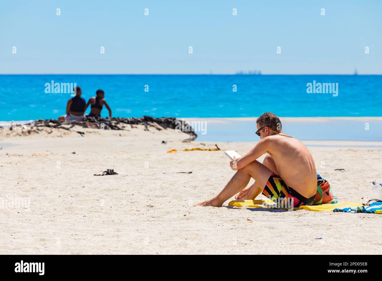 Cape Town, South Africa - February 19, 2023: Male vacationer reading a book on Camps Bay beach Stock Photo