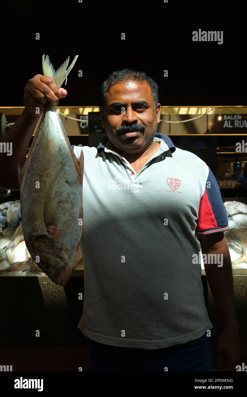 A vendor proudly holds up some fresh fish, catch of the day. At the