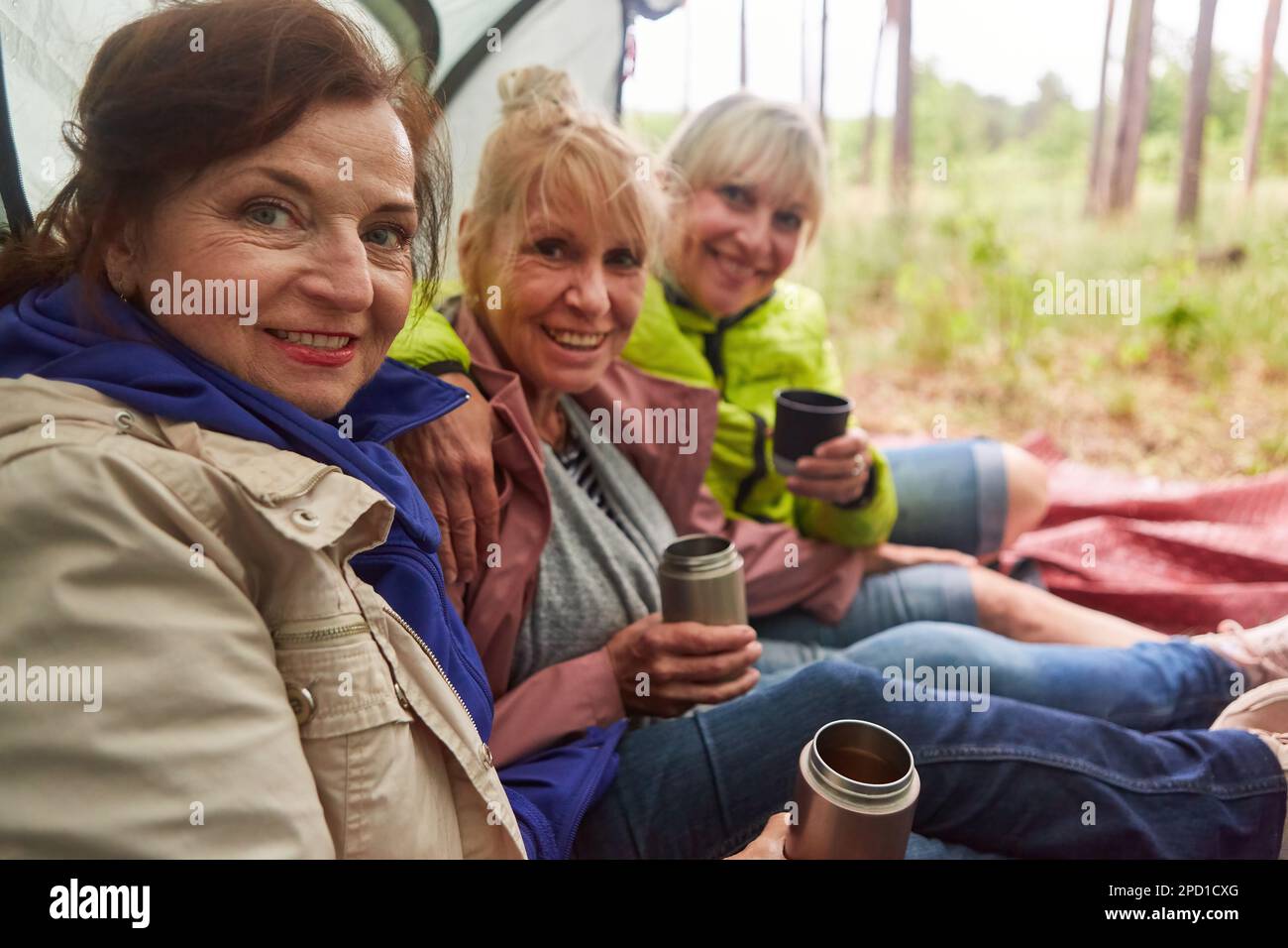 Portrait of smiling senior women having tea together while sitting in tent during camping Stock Photo