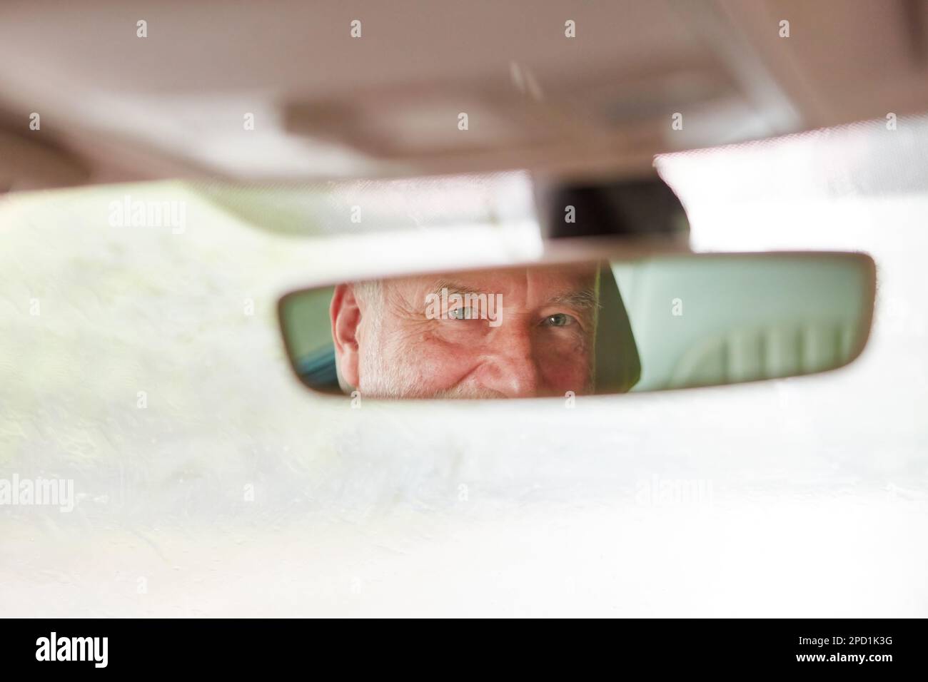 Reflection of elderly man on car's rear-view mirror during road trip Stock Photo