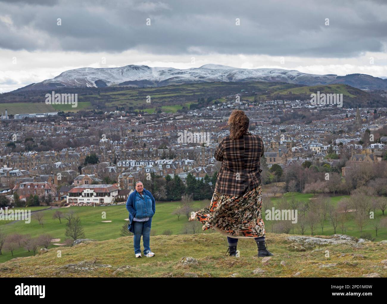 Cold and cloudy in Holyrood Park, Edinburgh, Scotland, UK. 14th March 2023. Temperature of 5 degrees centigrade with wind chill making the real feel of 0 degrees.Pictured: Tourists taking the opportunity to get a scenic view before getting back on the tourist coach. Credit: Archwhite/alamy live news. Stock Photo