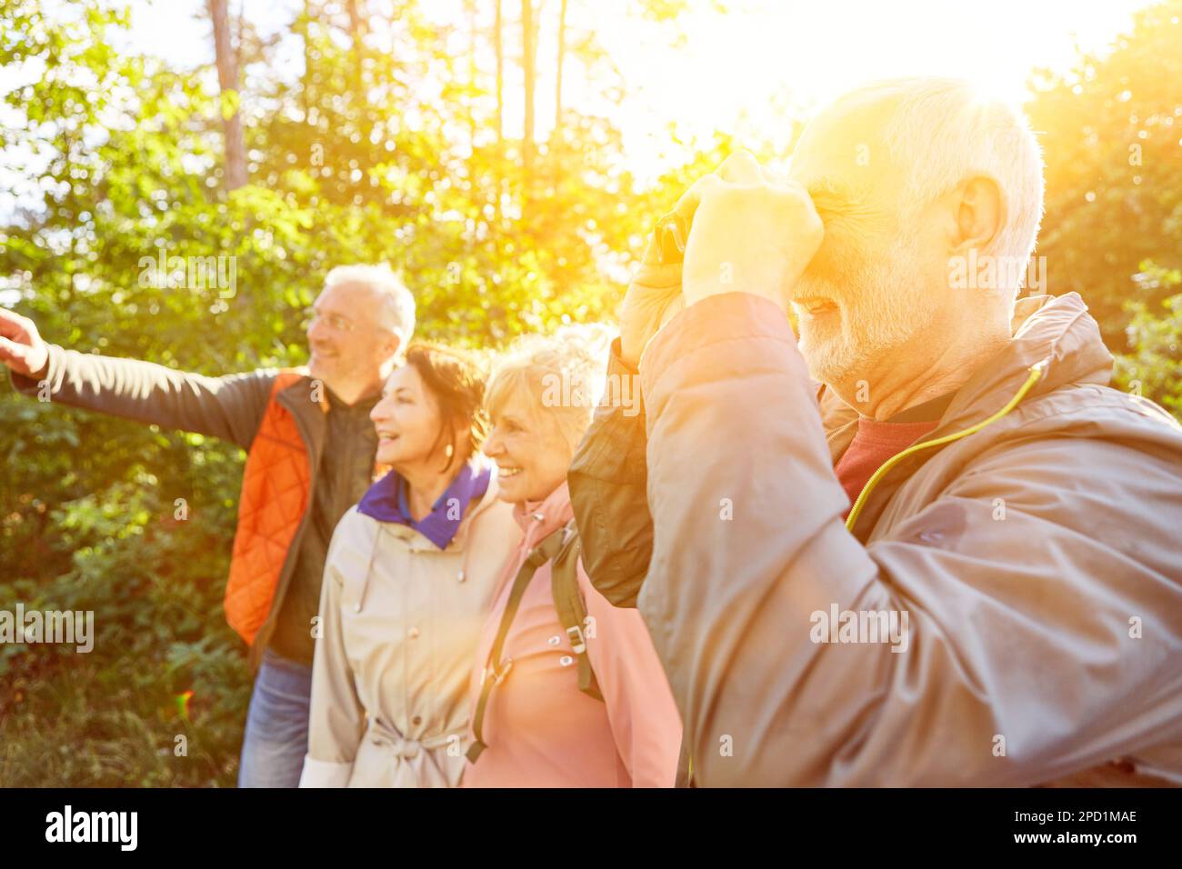 Happy elderly man bird watching through binoculars while exploring forest with friends during vacation Stock Photo