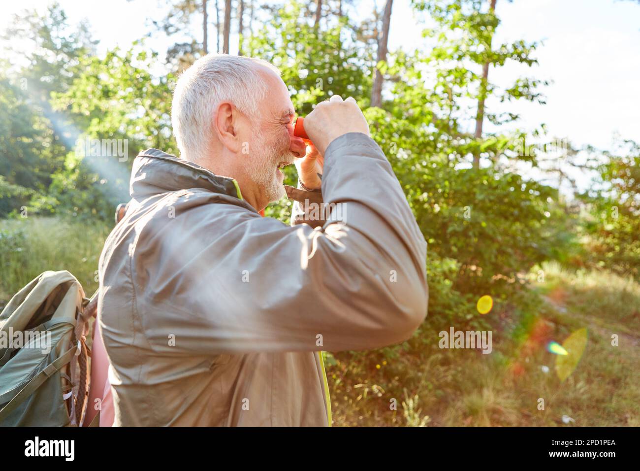 Happy senior man bird watching through binoculars while exploring forest during summer vacation Stock Photo
