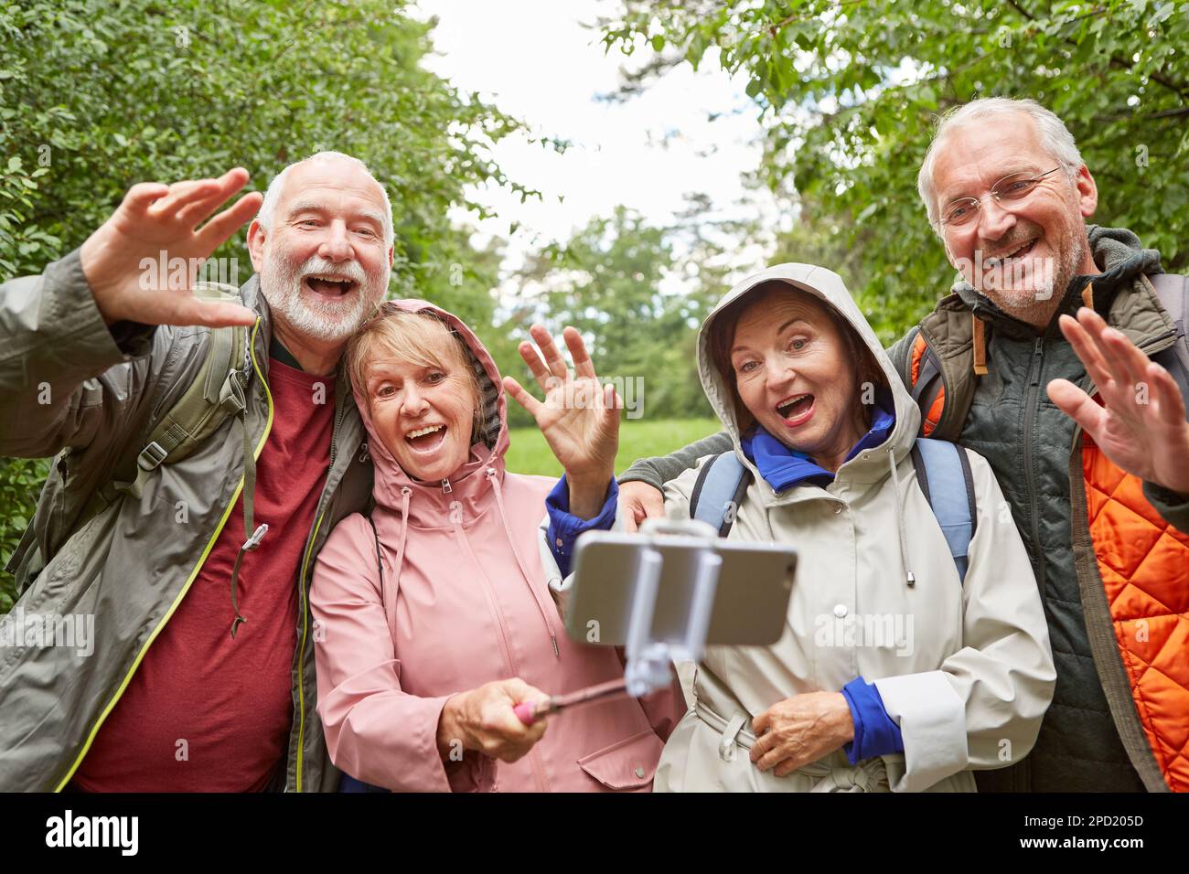 Cheerful senior couples waving on video call through smartphone in forest during vacation Stock Photo