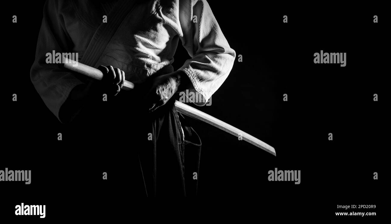 A person in black hakama standing in fighting pose with wooden sword bokken in black and white. Shallow depth of field. SDF. Stock Photo