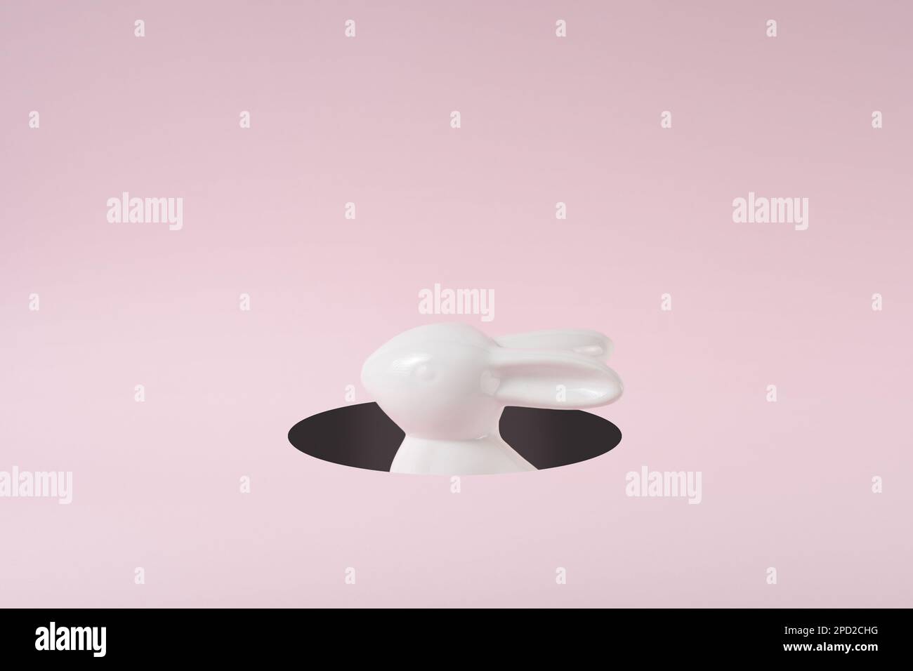 A white Easter bunny peeking out of a hole. Creative minimal concept. Stock Photo