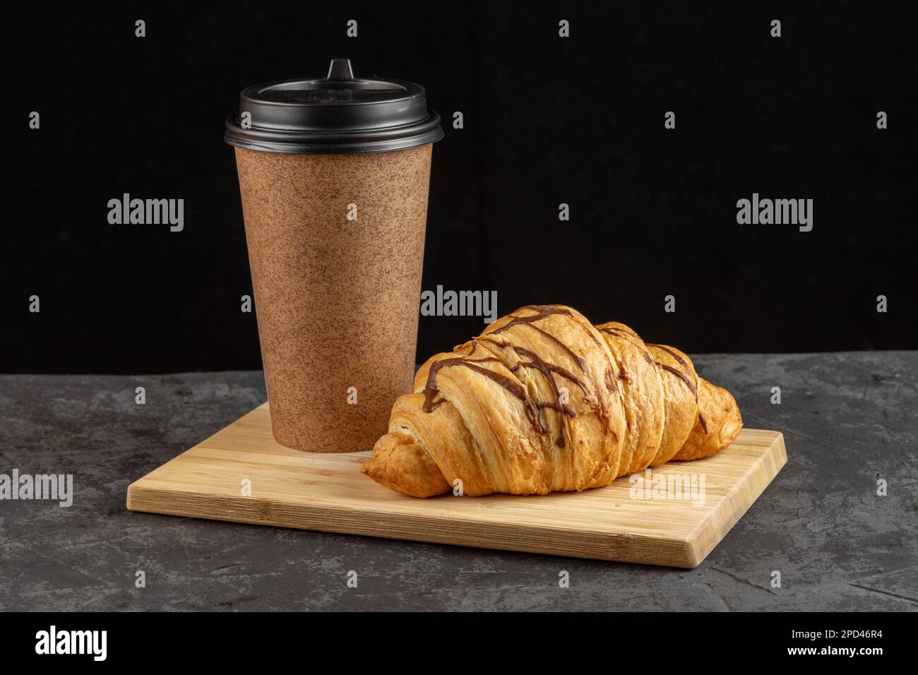 Paper cup with fragrant coffee and croissant on a dark background. Layout for design Stock Photo