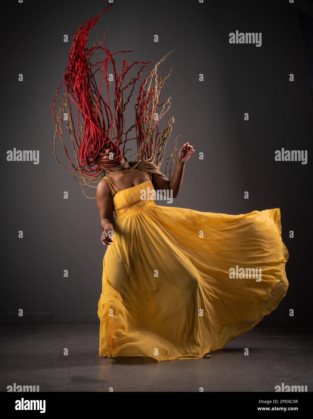 An African American female in a long, yellow dress displaying an energetic dance performance Stock Photo