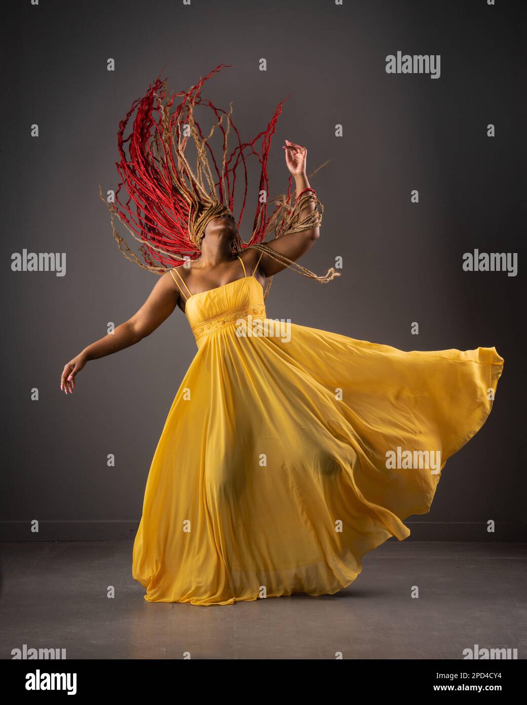 An African American female in a vibrant yellow dress dancing joyfully with moving hair Stock Photo