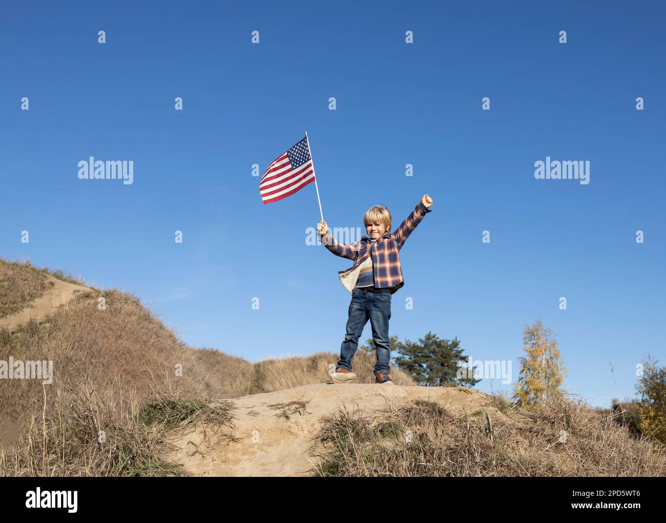 Patriotic boy 6 years old raised up hands holding the American flag against blue sky. Celebrate Independence Day of the United States of America. Prid Stock Photo