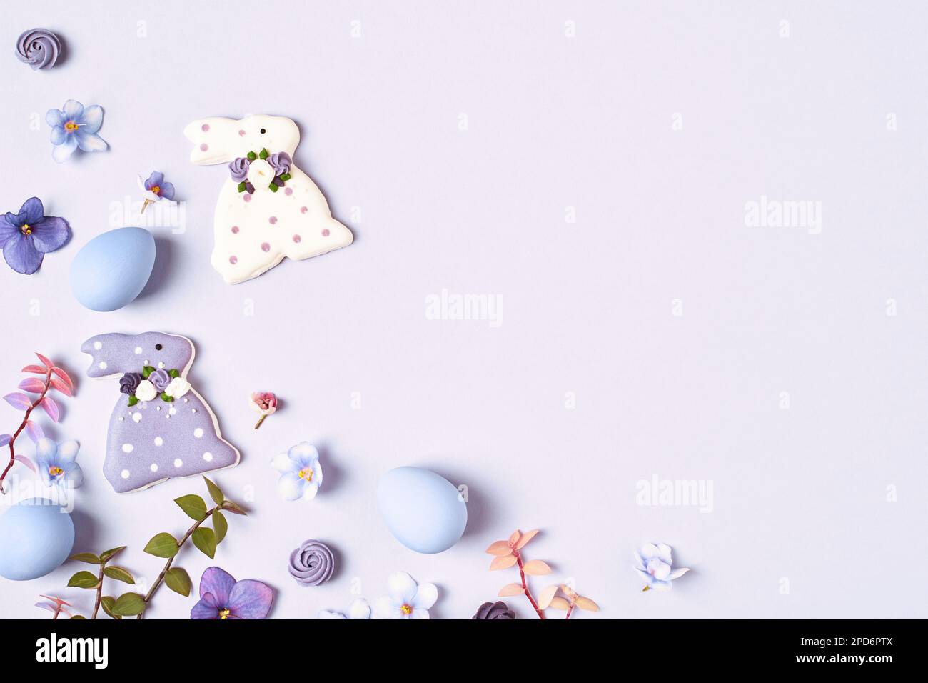 Easter background. Easter decorations, bunny, eggs and flowers on violet background. Copy space, flat lay. Corner frame. Stock Photo