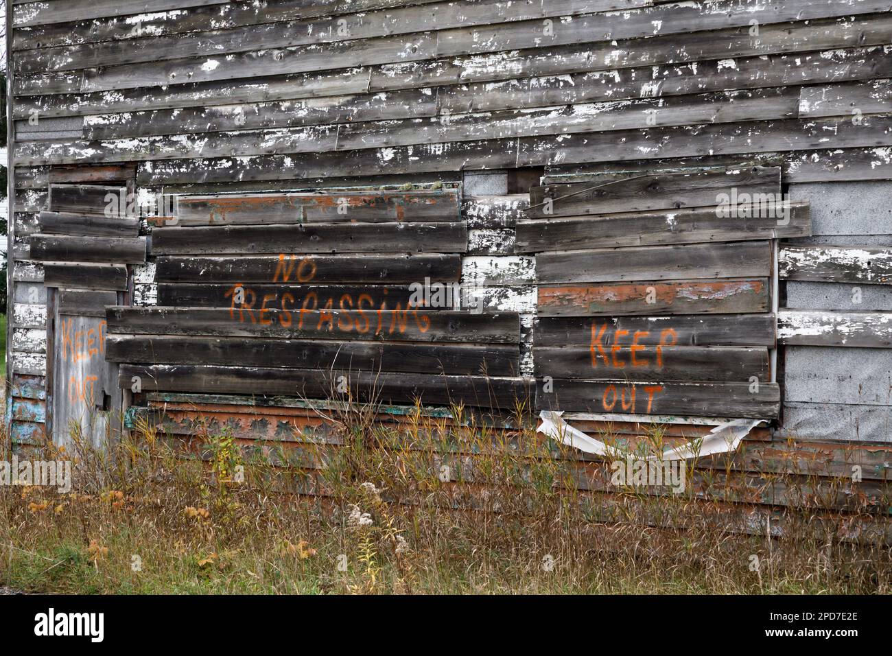 A keep out and no trespassing warning spray painted onto the side of an old weathered wooden building. Stock Photo