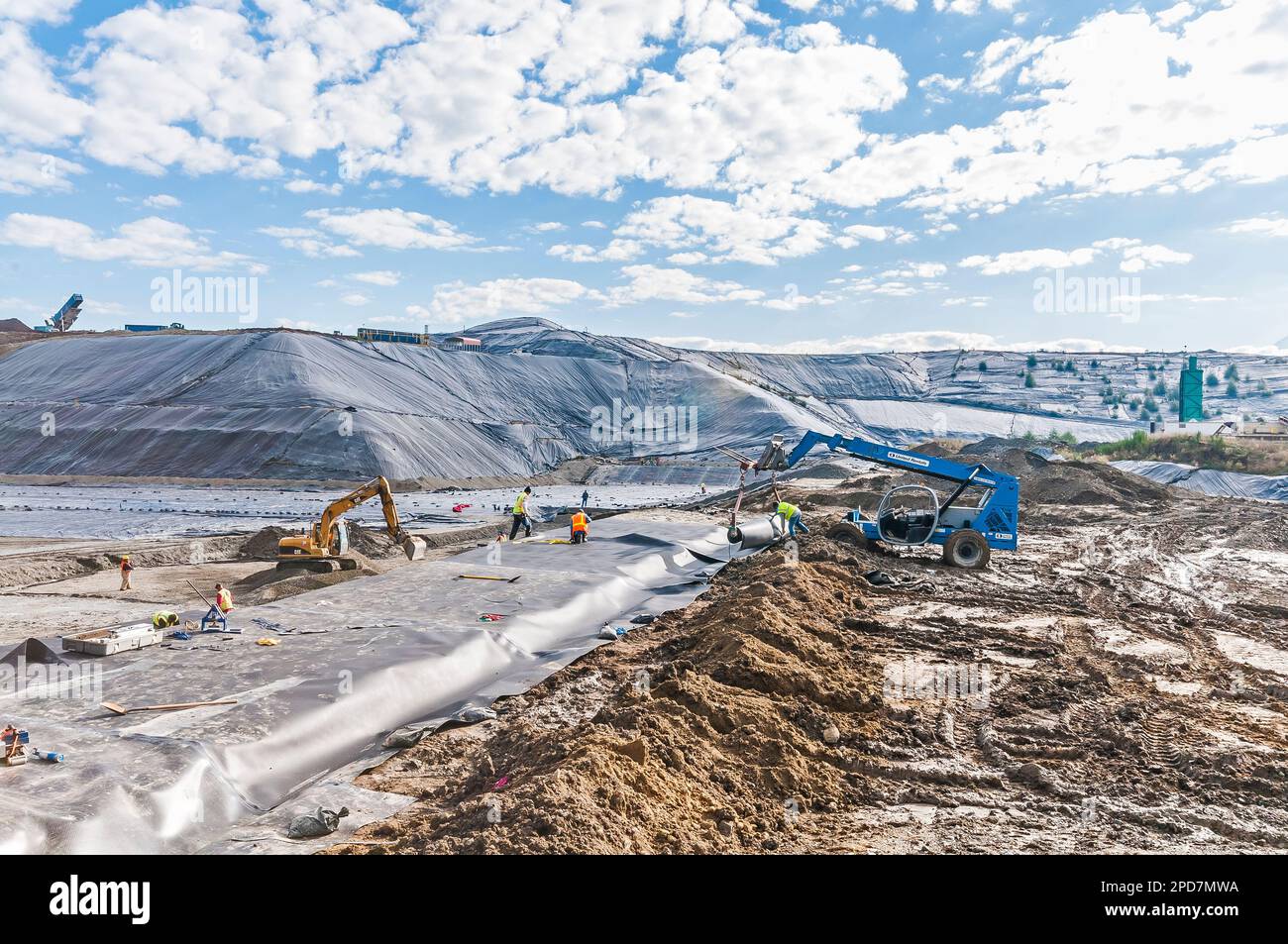 Workers with machinery are laying down plastic sheeting or geomembrane in an active landfill. Stock Photo