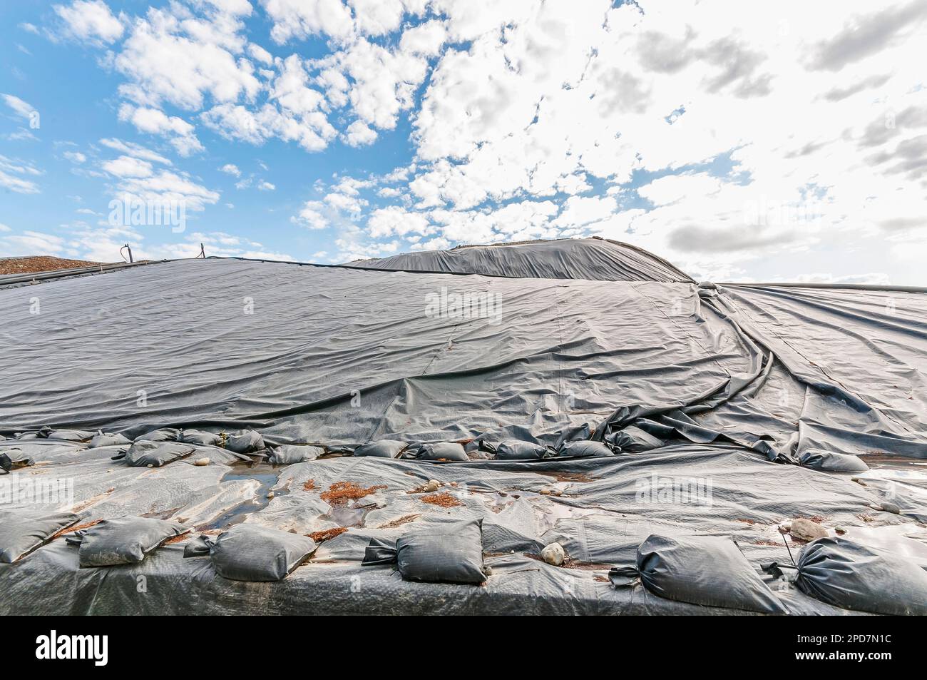 Plastic sheeting or geomembrane with sandbag weights cover hillsides in an active landfill. Stock Photo