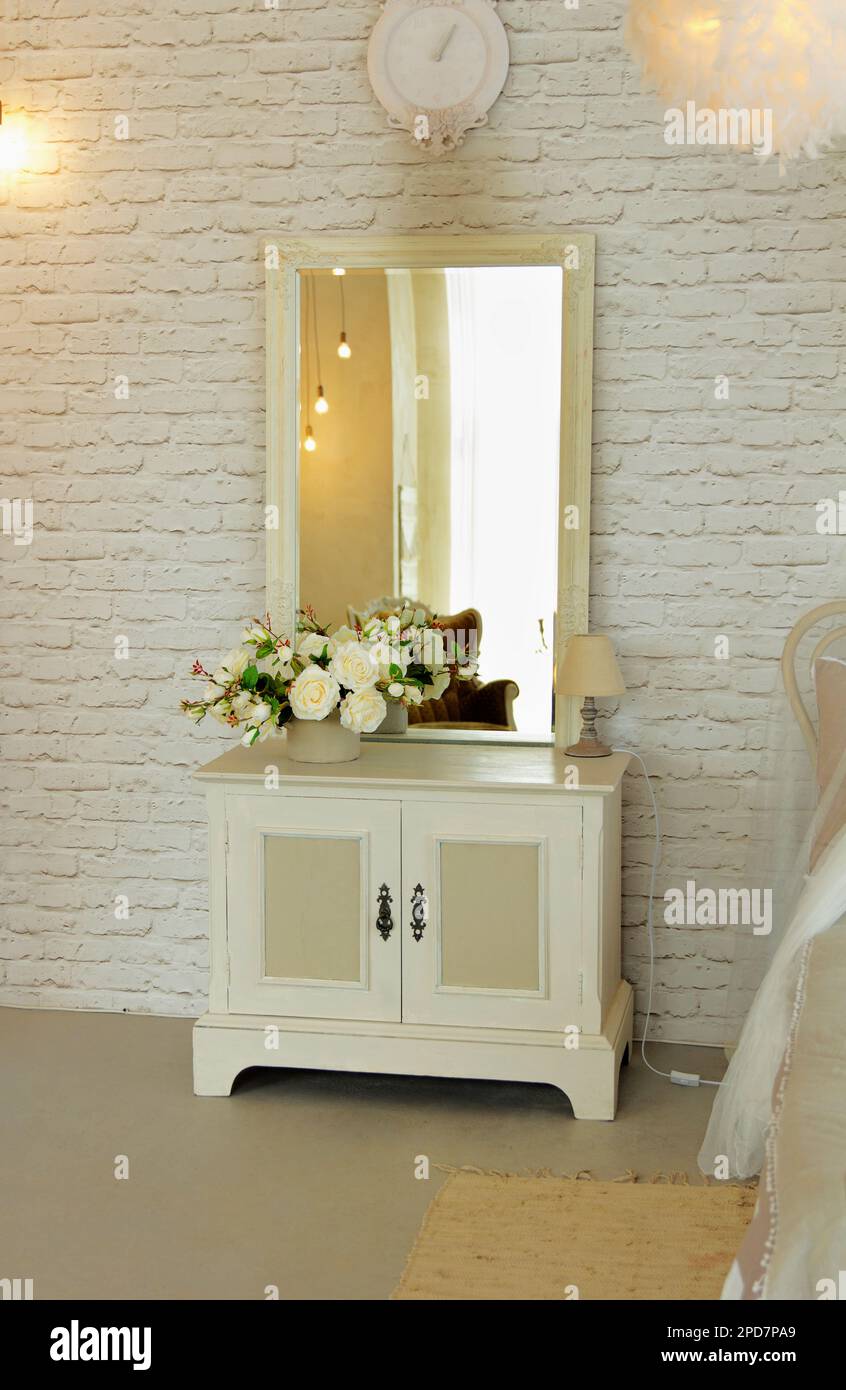 White elegant bedside table with square mirror located in bedroom as interior cosy room Stock Photo