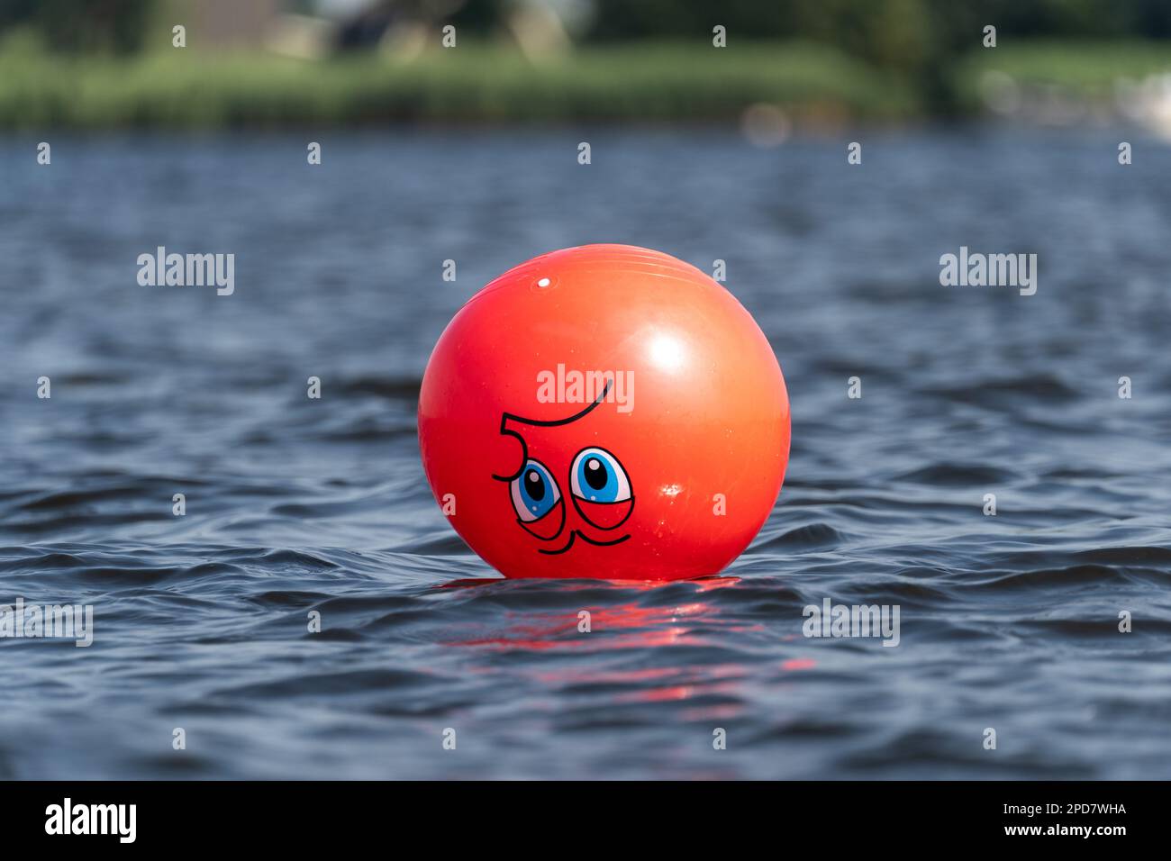 A floating red bal with a face floating upside down on the water Stock