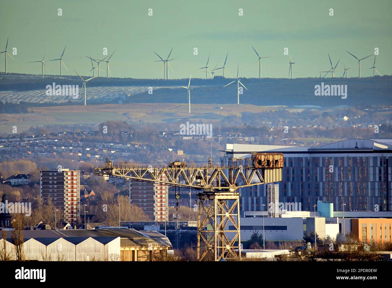 Glasgow, Scotland, UK 14th March, 2023. UK Weather: Snow overnight  and sleet showers ended and a sunny late afternoon saw the city bathed in light.Old and the new as the former clyde totan shipbuilding crane is lofted over by the whitlee wind farm to the south. Credit Gerard Ferry/Alamy Live News Stock Photo