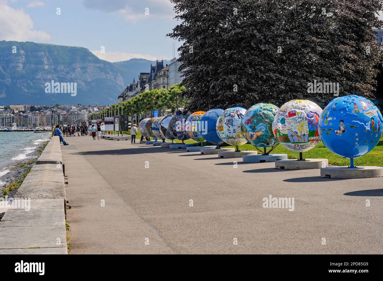 A row of statues in forms of world globes displayed outdoors in the sunny park near body of water Stock Photo
