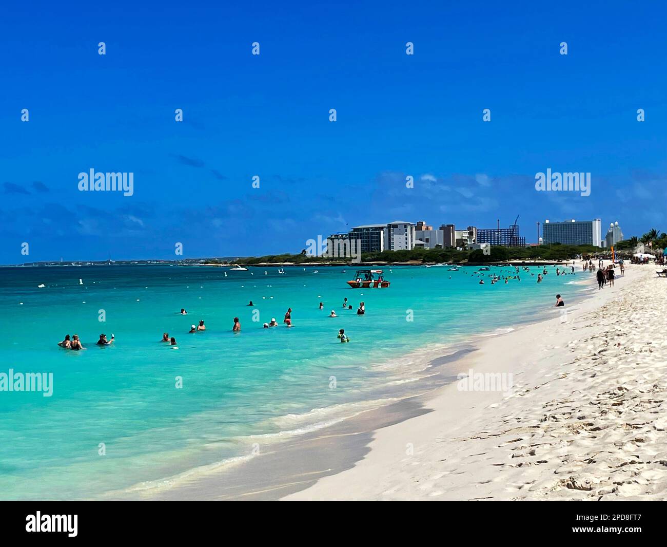 Eagle Beach, Oranjestad, Aruba, March 10, 2022. People on the beach and in the water. Hotels and resort buildings in the background. Stock Photo