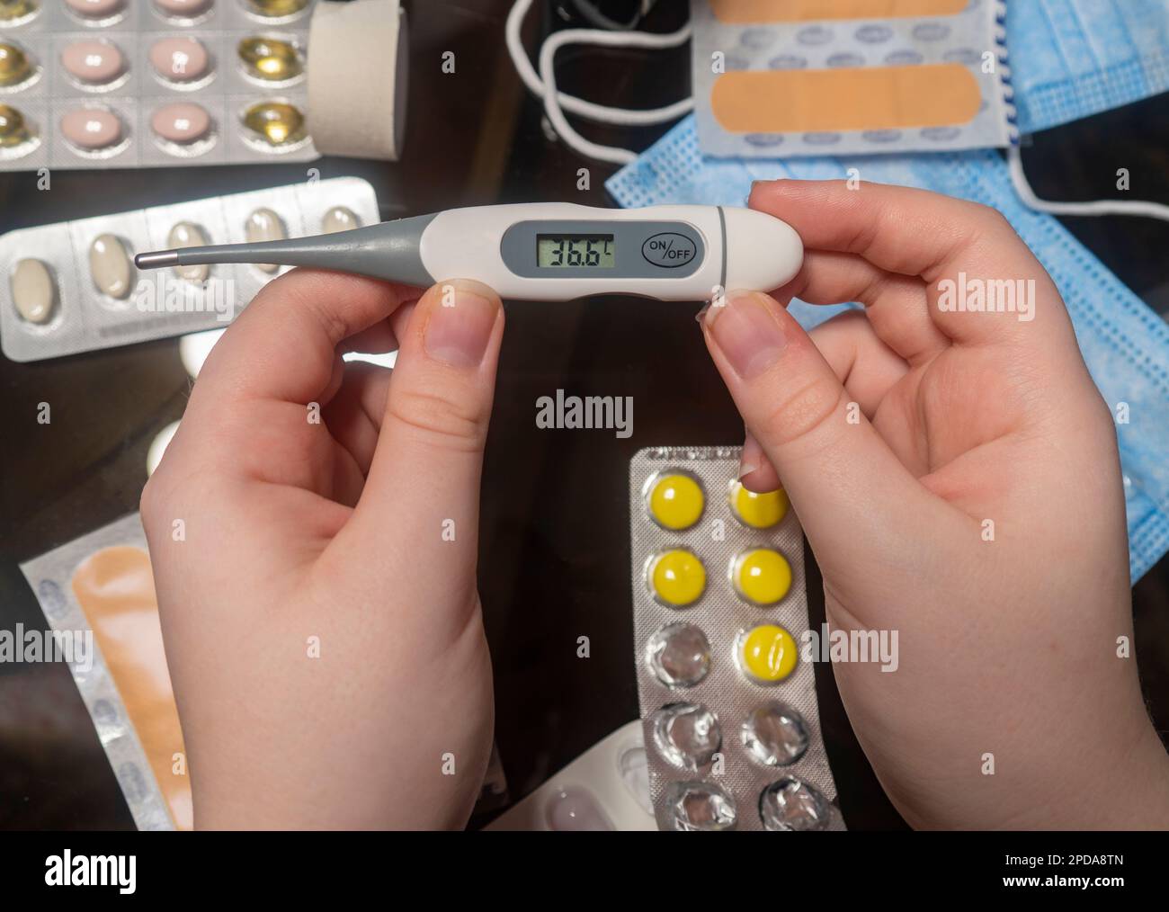 Electronic thermometer in hands against background of a table with medicines (close-up). Concept of medicine, pharmacy, healthcare and home treatment Stock Photo