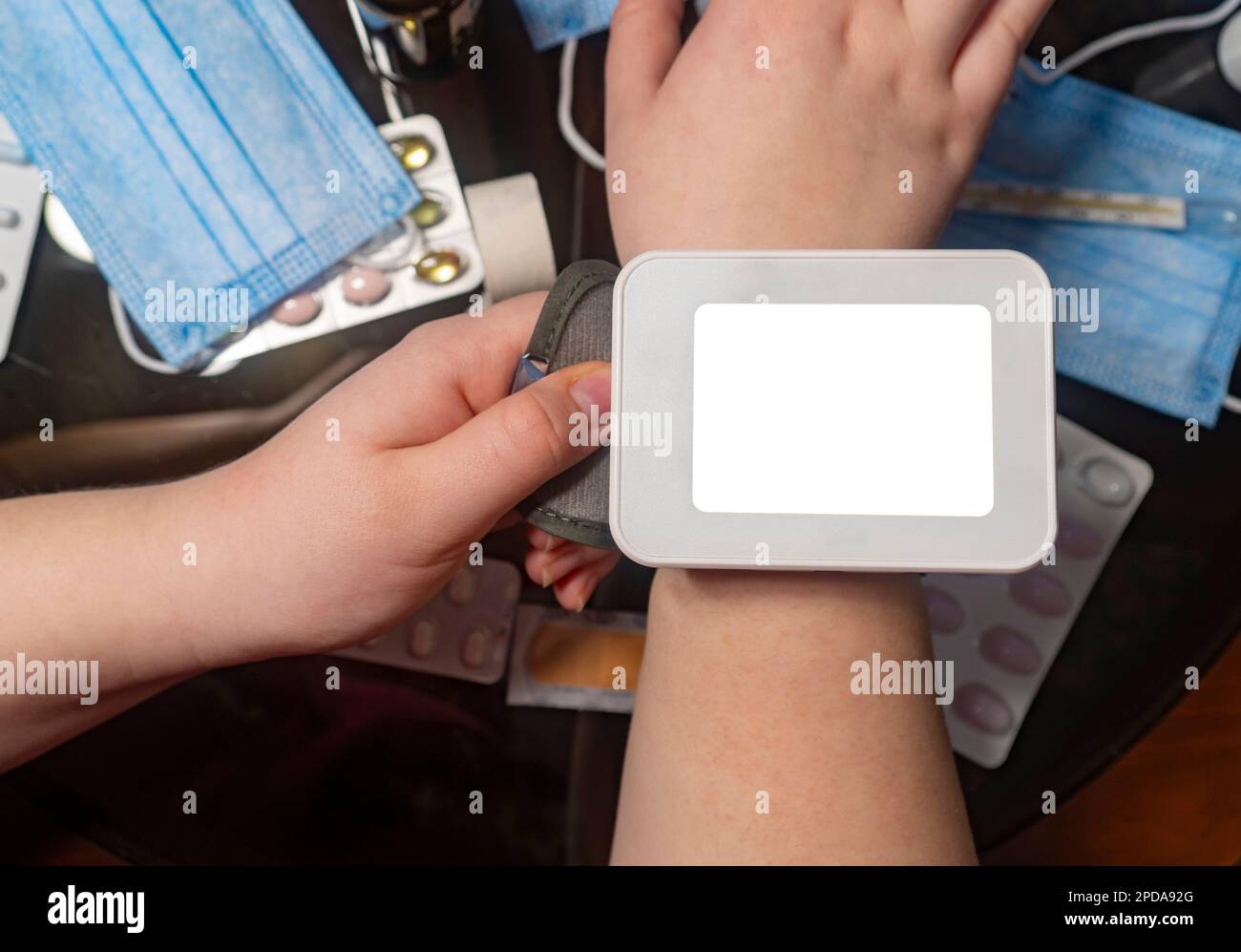 Blood pressure monitor with a clean screen on arm against background of a table with medicines (close-up). Concept of medicine and home treatment Stock Photo
