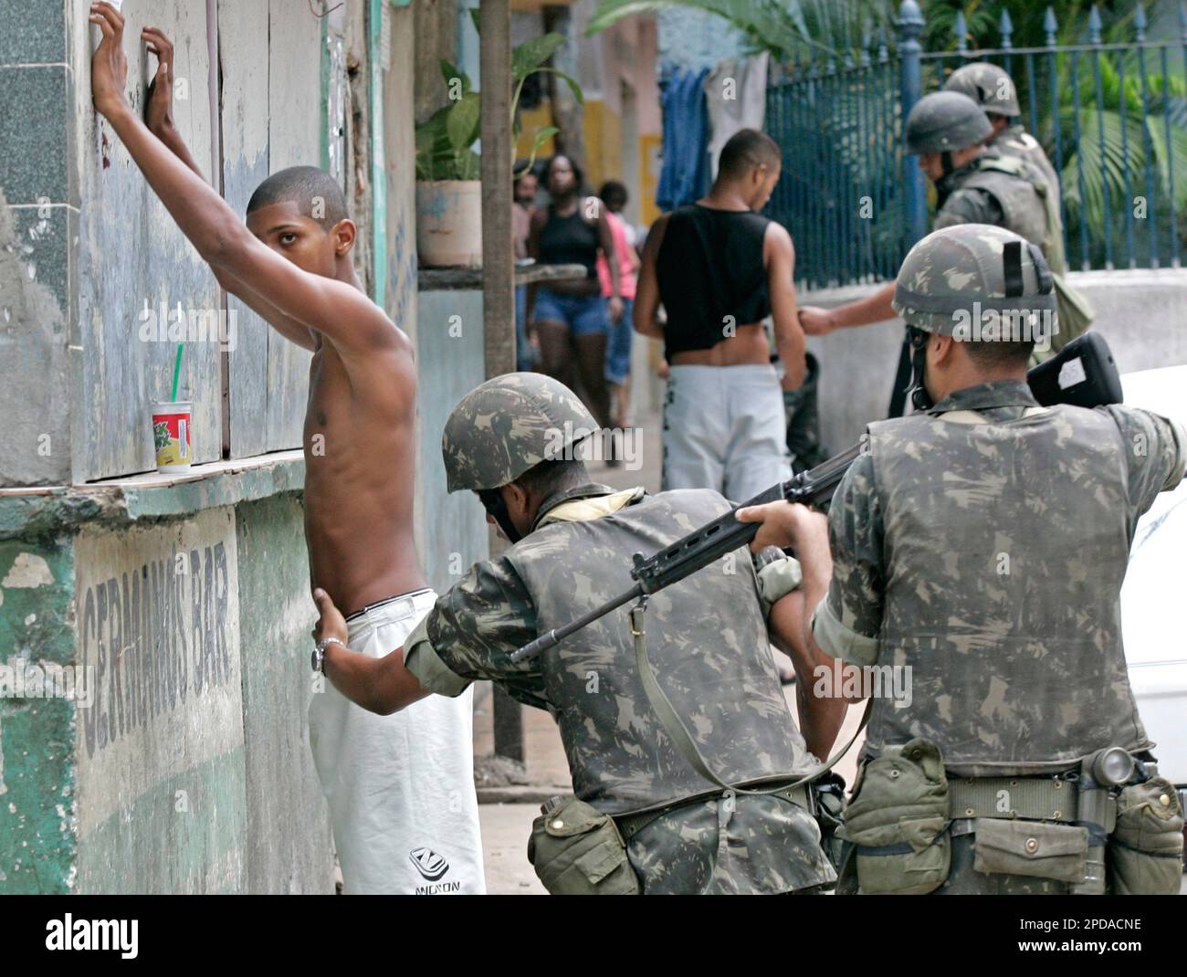 Brazilian soldiers search a man looking for guns at the entrance