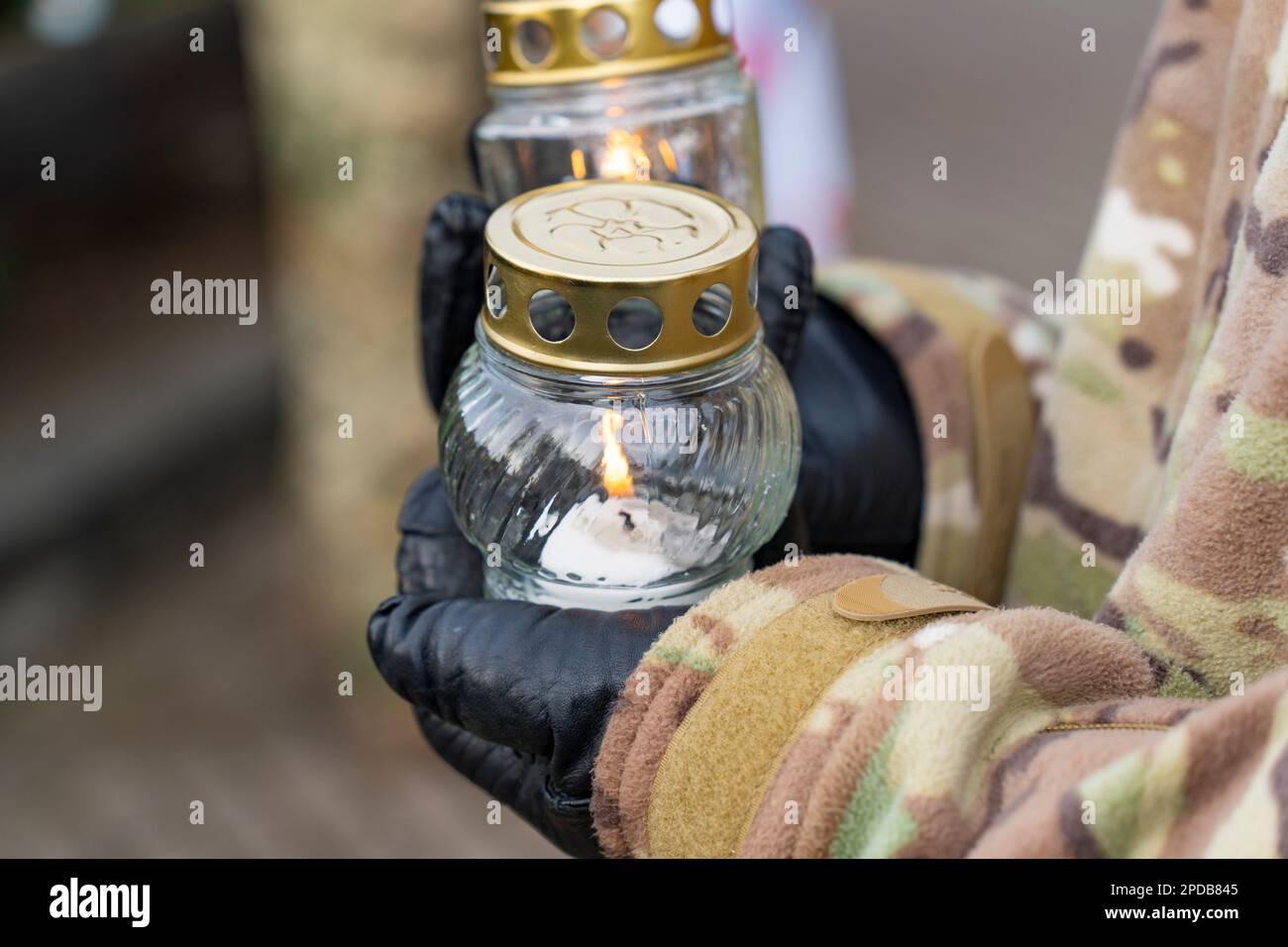 A soldier in camouflage and black gloves holds candlesticks at a military commemoration Stock Photo