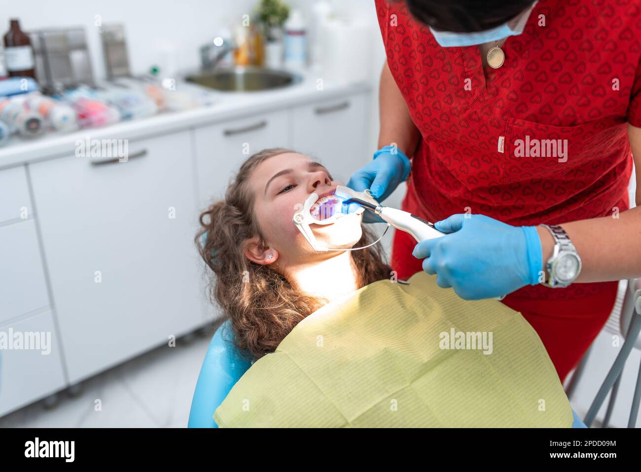 The dentist uses an ultraviolet lamp while fitting the girl with braces
