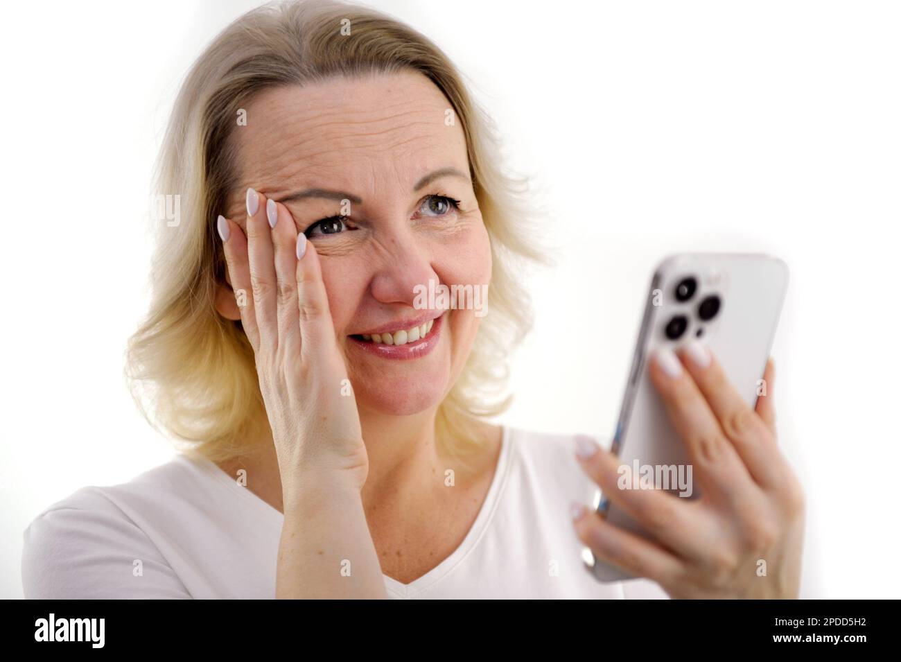 Surprised young pretty European female with long blonde hair covering mouth with hand and looking at her phone, receives sms, posing on soft violet background Human emotions, reaction Stock Photo