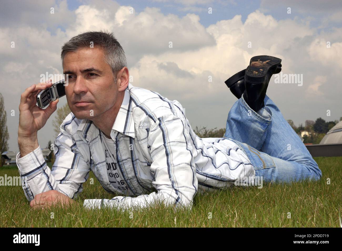 elderly man lies in prone position in a meadow and talking on his mobile phone Stock Photo