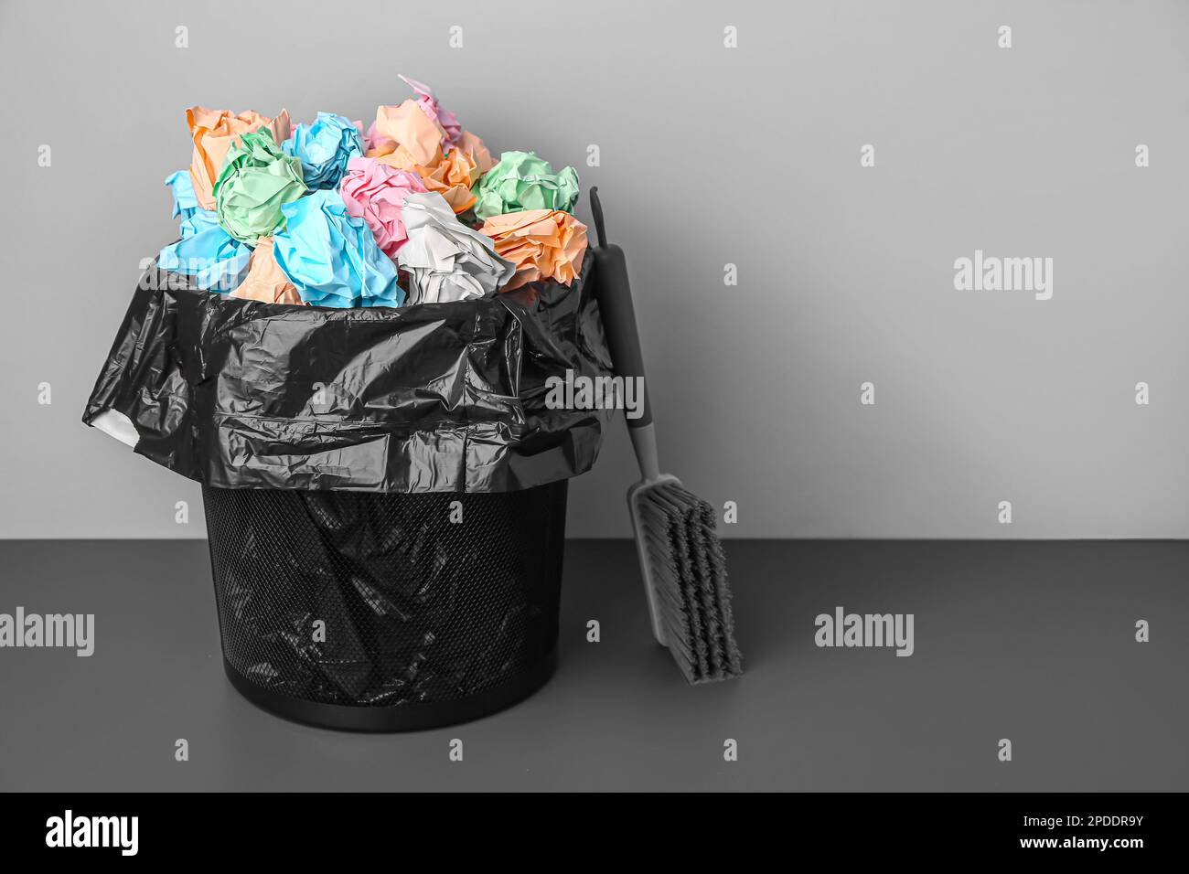 Rubbish bin with crumpled paper and brush near grey wall Stock Photo