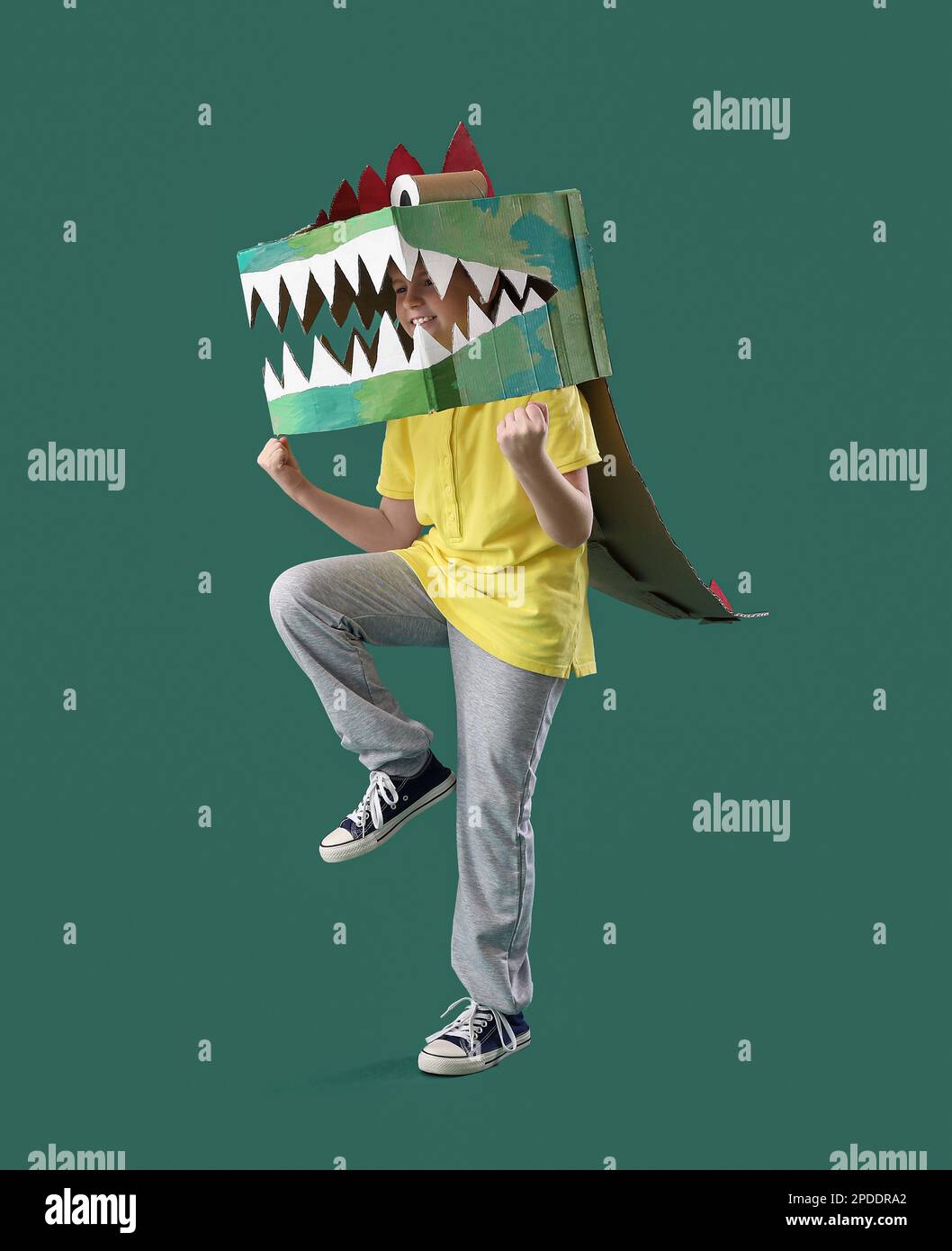 Little boy in cardboard dinosaur costume on green background Stock
